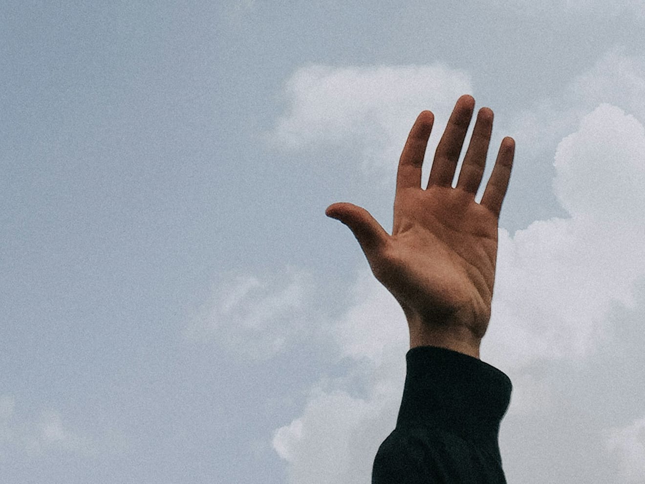 A photo of a hand raised into the air against a cloudy sky. 